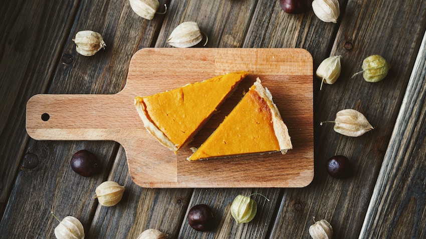 Two slices of pumpkin pie on a wooden chopping board