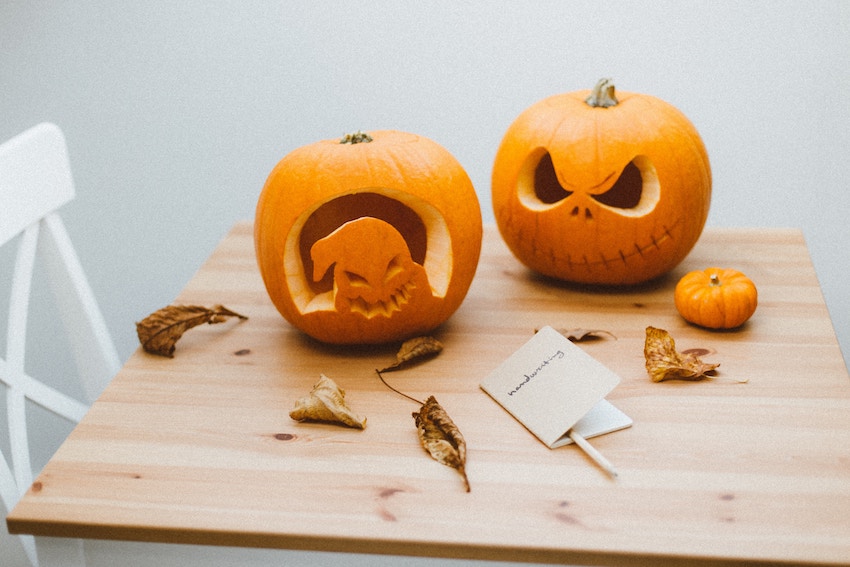 Three pumpkins on a table. Two are carved for Halloween, one with a ghost face and one with menacing eyes. The third pumpkin is very small.