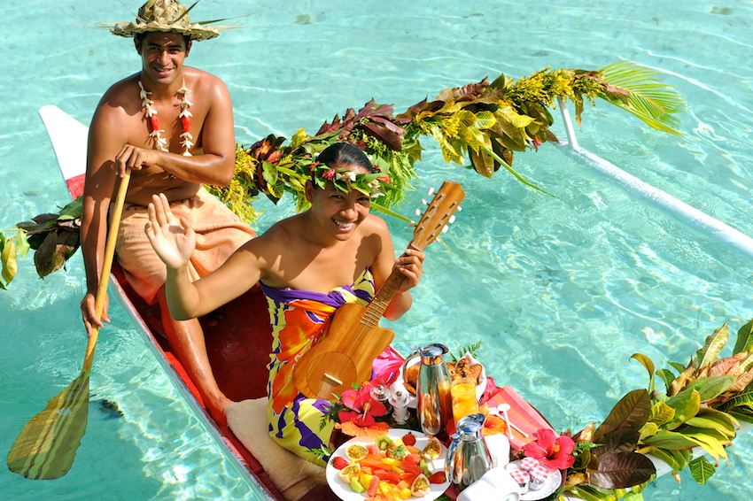 Tahitian couple enjoying fruit breakfast in a wooden canoe