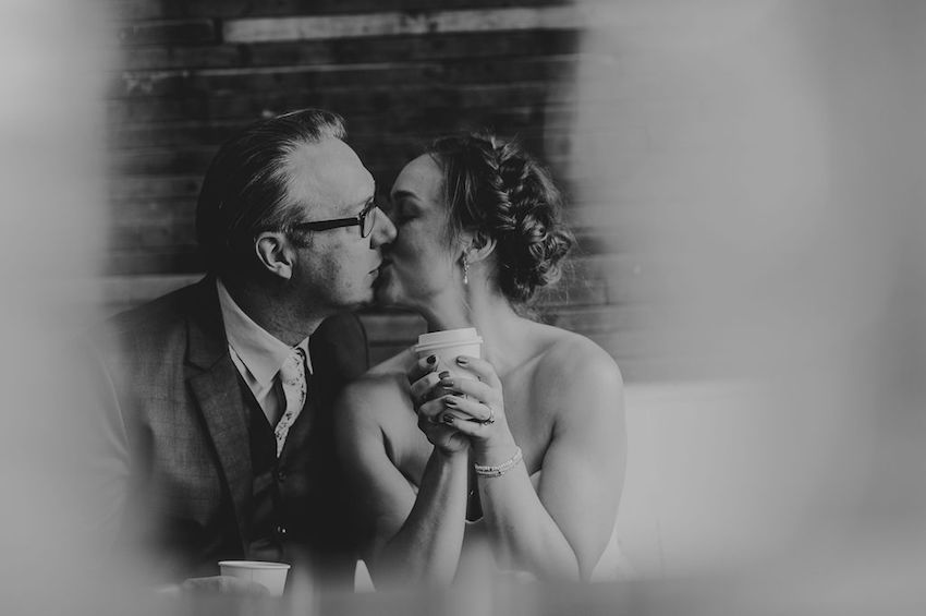 B+W image of Bride and Groom kissing while holding coffee