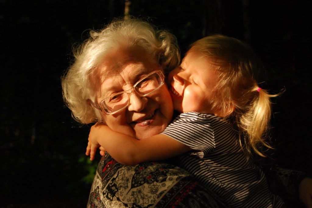 Young girl with blond hair hugging her grandmother in the sunshine