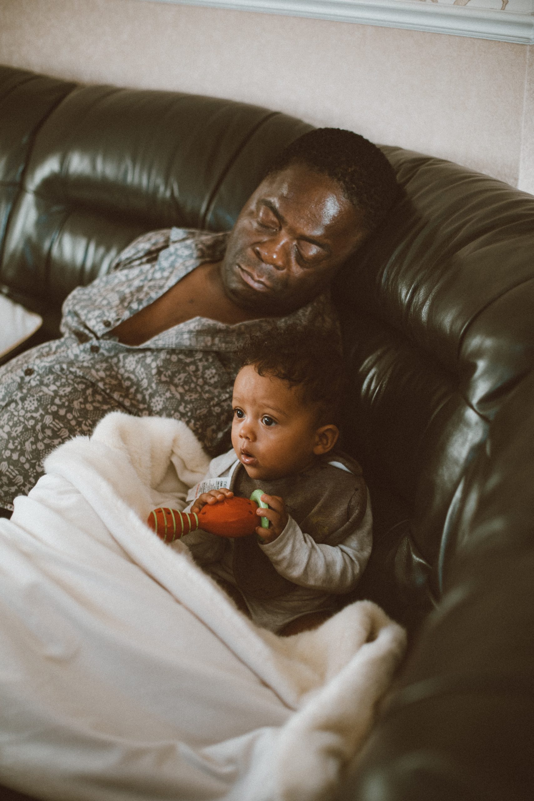Young toddler sitting on sofa next to his sleeping grandfather