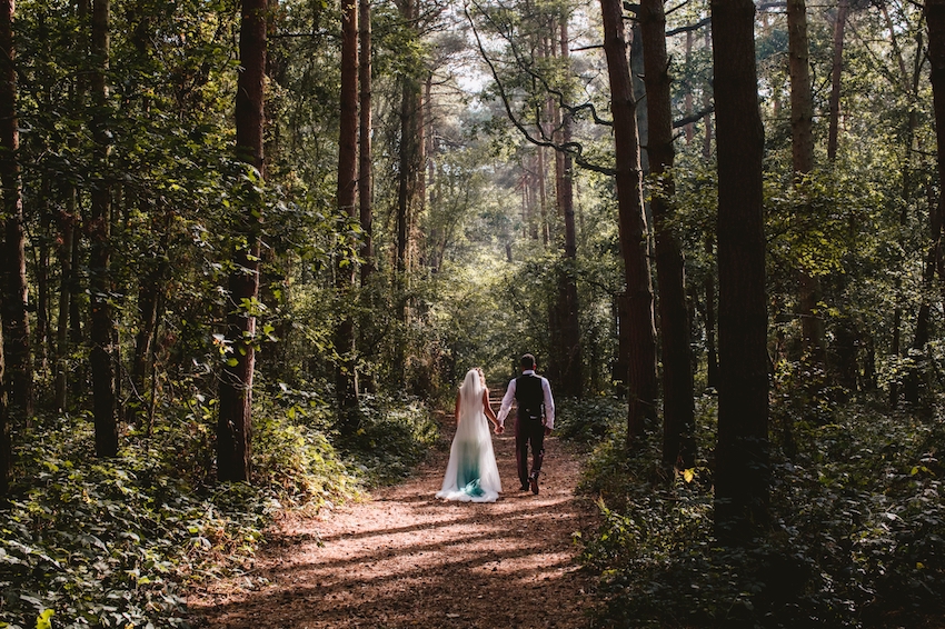 Photo of couple on wedding day, from behind, walking through forest holding hands