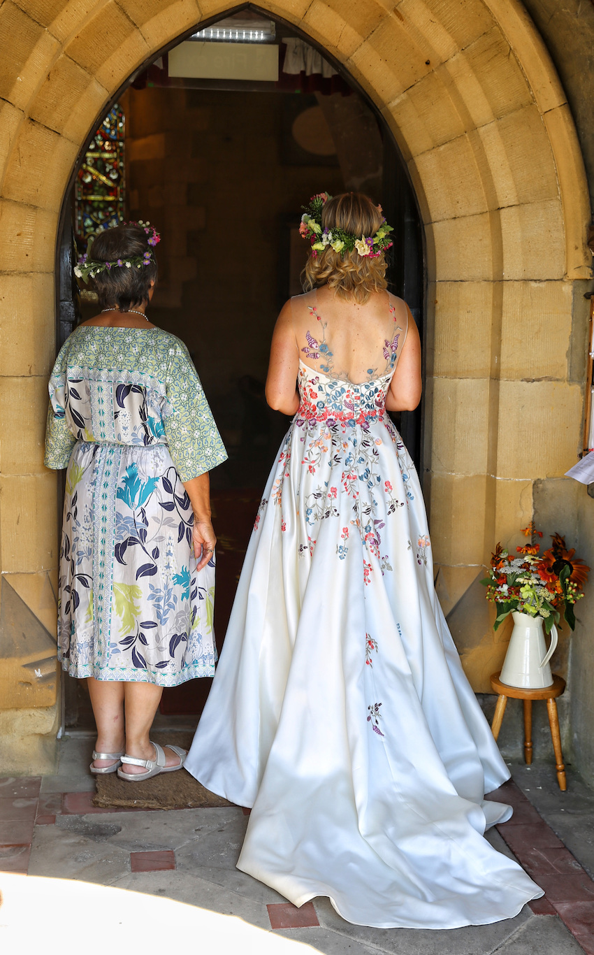 Bride and her mother, standing with backs to camera at entrance to village church