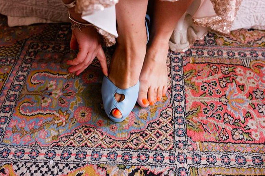 Bride putting on a pale blue open toe show against an dusky oink patterned rug