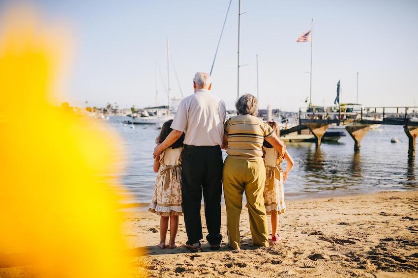 grandparents standing on edge of shoreline looking our to sea with their arms round their grandchildren