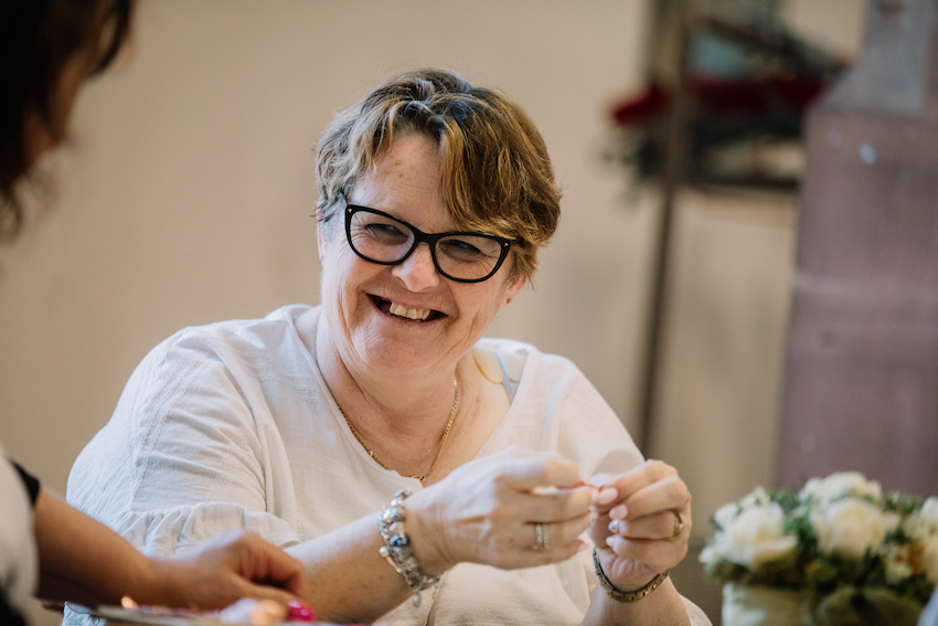 mature white woman wearing glasses and with short dark blonde hair, laughing with someone off camera